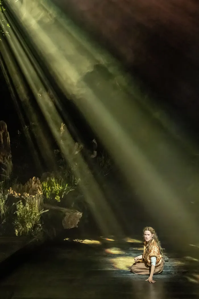 Shafts of light fall on a lone figure in the woods, Into the Woods at the Bridge Theatre